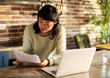 © Davor - Woman reviewing bills on laptop in home kitchen
