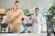 © JackF - Modern pregnant woman using phone to scan QR code on bottle of syrup and check ingredients or reviews online, while polite pharmacist preparing to offer professional advice or alternative in pharmacy