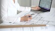 © volha_r - Architect working on building blueprint plans, designing new residential or commercial real estate projects for construction, using a ruler and laptop on a desk