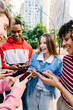 © Xavier Lorenzo - Young friends smiling while checking phones outdoors. Students enjoying online interaction and social media together. Technology and lifestyle concept.