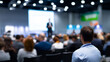 © Curioso.Photography - Audience attending business conference with speaker on stage in blurred background highlighting professional event atmosphere