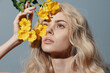 © VICHIZH - Ethereal blonde model with golden flowers against a blue backdrop, exuding serenity and beauty in a soft summer vibe.