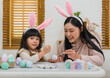 © geargodz - mother and preschool child girl wearing bunny ears painting and decorating egg  together at home on easter day. happy family holiday activity concept