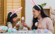 © geargodz - mother and preschool child girl wearing bunny ears holding colorful egg while celebrating together at home on easter day. happy family holiday activity concept