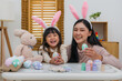 © geargodz - mother and preschool child girl wearing bunny ears holding colorful egg while celebrating together at home on easter day. happy family holiday activity concept