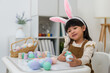 © geargodz - happy preschool child girl wearing bunny ears holding colorful egg while celebrating on easter day on table at home