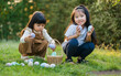 © geargodz - two happy child girl playing together and hunting for Easter eggs into basket on green grass in garden