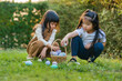 © geargodz - two child girl playing together and hunting for Easter eggs into basket on green grass in garden