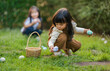 © geargodz - two child girl playing together and hunting for Easter eggs into basket on green grass in garden