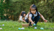 © geargodz - two child girl playing together and hunting for Easter eggs into basket on green grass in garden