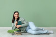 © Pixel-Shot - Young woman with books lying on floor near green wall