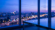 © Chari - A glass table sits in the foreground of a blurred cityscape at dusk, with lights from buildings and traffic creating a bokeh effect.