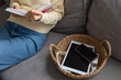 © juliasudnitskaya - Digital detox concept from woman reading paper book while phone and tablet gadgets lying offline in basket. Home and mental leisure instead social media and technology addiction.