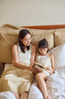 © Blue Jean Images - Mum and daughter lying on bed, reading books