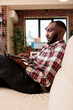 © DC Studio - Male freelancer working on laptop at home, doing remote job and sitting on couch. Person using computer to work on startup presentation with data research, sending business email.