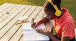 © Running opossum - young girl with headphones studying outside at a wooden table on a sunny day