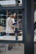 © qunica.com - Two female professionals review documents while standing in a modern office. They discuss work and collaborate through a glass partition in a contemporary workspace.