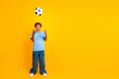 © deagreez - Young boy in blue shirt and jeans tossing a soccer ball against a bright yellow background