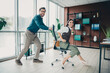 © deagreez - Two colleagues in a modern loft office share a playful moment as a man pushes a woman in a chair while smiling creating a lively scene of teamwork in the workplace