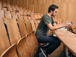 © Connect Images - Man in green shirt using tablet in an empty lecture hall with wooden seats. Germany