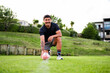 © NZstockphoto - Samoan man in activewear kneels on a green sports field, ready to kick a rugby ball