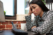 © DC Studio - Closeup of exhausted entrepreneur resting her face on her palm at desk after a long workday. Businesswoman with hand on forehead trying to stay alert while working on computer in a startup office.