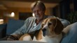 © forenna - Elderly widower video calls distant family while aging beagle rests head on knee in dimly lit living room, perfect for digital connection, remote communication keywords, and contemporary technology