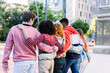 © Xavier Lorenzo - Group of diverse young people with arms around each other walking away from the viewer in a modern urban park, expressing concepts of friendship, unity, and support
