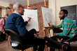 © DC Studio - Two diverse men art school students talking during lesson, sitting at easels discussing artwork during creative group class, friends learning basics of drawing and sketching together