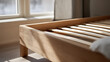 © A2Z AI  - Minimalist wooden bed frame with slat base bathed in warm sunlight near a window, showcasing natural light and cozy home interior