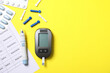 © New Africa - Diabetes. Digital glucometer with test strip, pen, lancets, pills and record form on yellow background, flat lay. Space for text