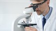 © rogerphoto - Adult male scientific researcher analyzing sample through microscope, wearing protective gear in high tech laboratory environment. Healthcare, medicine and science concept