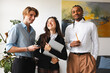 © Studio Marmellata - A diverse group of three young professionals, two men and one woman, share a moment of laughter and collaboration in a modern office setting.