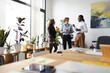 © Studio Marmellata - Three colleagues in a modern office setting are engaged in a conversation while holding beverages, surrounded by plants and artwork.