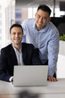 © fizkes - Team portrait two smiling multiethnic businesspeople ceo mentor and coworker trainee enjoying successful collaborative achievement productive coaching session at office desk by laptop. Vertical shot