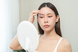 © KMPZZZ - Anti aging, worry puberty asian young woman, stressed girl looking in mirror, allergy presenting an allergic reaction from cosmetic on face. Beauty, health care from acne problem, dry skin, treatment.