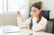 © KMPZZZ - Eye problem concept, fatigue asian young woman tired eyes, irritated rubbing nose dry relief vision pain after work on laptop computer, eye strain, put glasses on table, suffer migraine, bad blurry.
