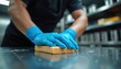 © Pete - Worker wears blue gloves, cleans steel counter with sponge. Focuses on hygiene in commercial kitchen setting. Professional sanitation for food safety standards.