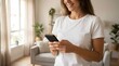 © Yassine - Smiling Woman Engaged with Mobile Phone in Bright Living Room, Embodying Modern Digital Connection and Casual Home Lifestyle