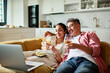 © Marko Geber - Happy couple watching laptop and drinking wine on sofa at home