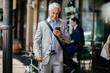 © Marko Geber - Senior businessman with bicycle using smartphone outside city cafe