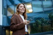 © Jelena - Professional woman smiling, holding smartphone in city