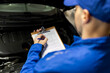 © zphoto83 - Auto mechanic filling maintenance checklist beside open car engine bay