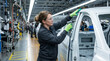 © ViskBx - Female automotive worker using electric drill to assemble car body frame on assembly line in modern car factory