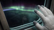 © lacindex - Astronaut glove touching spacecraft window glass against blurred glowing green aurora borealis space background