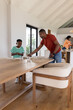 © wavebreak3 - African American family arranging tableware at home with man in orange T-shirt leaning over table