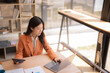 © Tj - Asian businesswoman focused on budget and financial reports, working with laptop and calculator at a modern desk, analyzing data, charts and paperwork in a bright office