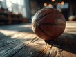 © Alexei - Close-up of a worn basketball resting on a wooden floor in a spacious gymnasium with natural light streaming through large windows