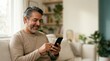 © Николай Срибяник - Senior man smiling while using smartphone on sofa in modern living room.