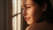 © Future Vision - Gazing adult female showing bare shoulder and dewy skin by window, sunlight creating muntin shadows